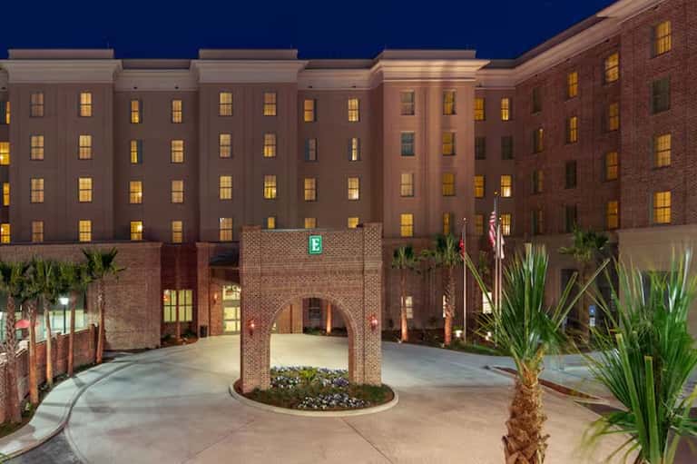 Illuminated brick hotel building at dusk with courtyard entrance and palm trees