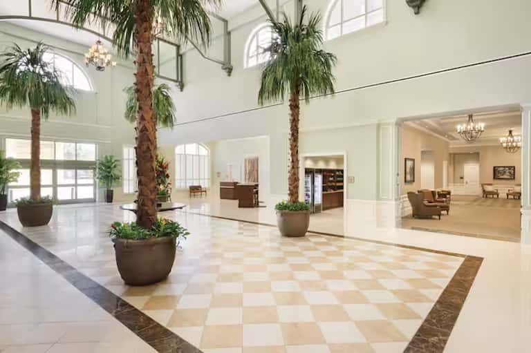 Grand hotel lobby with soaring ceilings, tall palm trees in planters, and checkered marble flooring