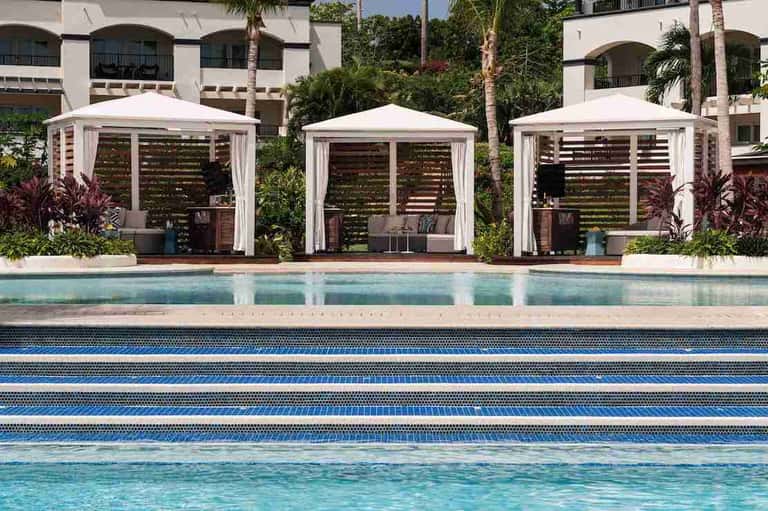 Three white cabanas with louvered privacy screens beside an outdoor lap pool