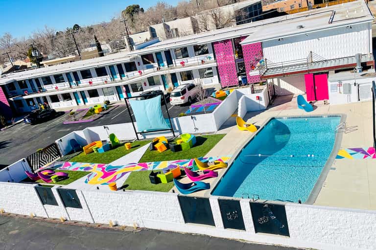 Colorful modern resort pool area with vibrant pink accents, geometric art installations, and poolside cabanas