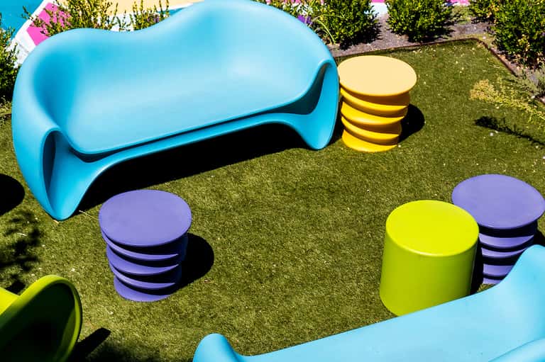 Colorful modern seating area with blue bench, yellow and purple stools on artificial turf