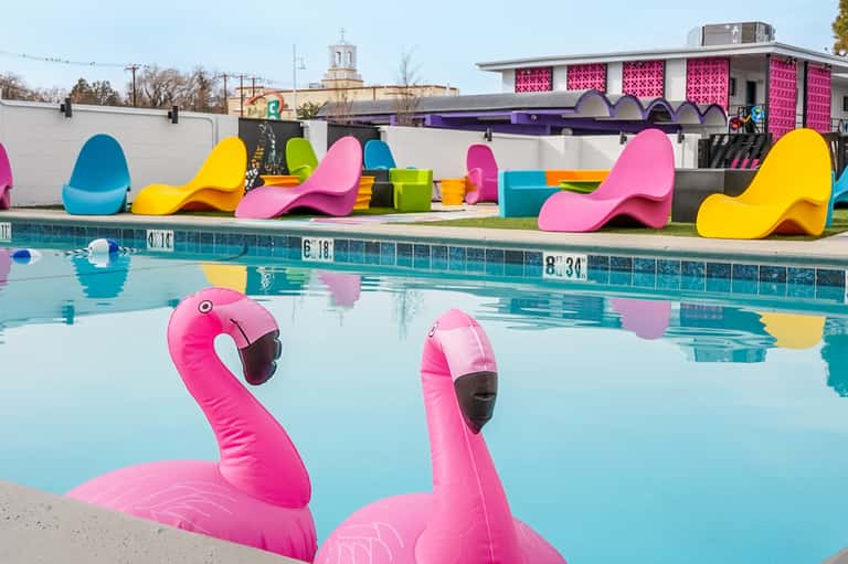 Colorful pool with pink flamingo floats, neon-colored loungers, and vibrant poolside decor