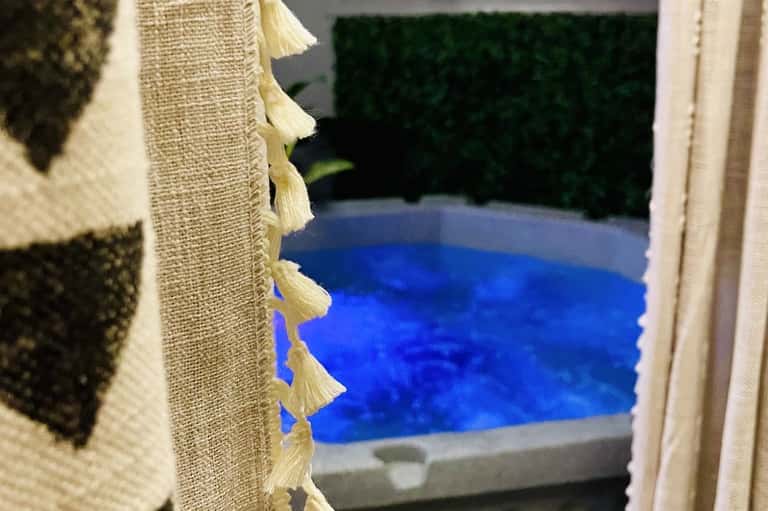Luxury hot tub with cream and taupe striped towel draped over edge, blurred pool background