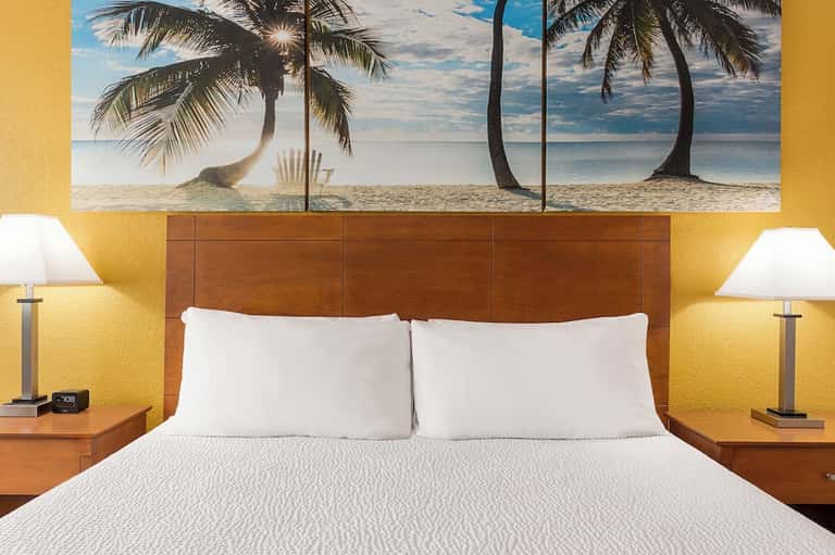 Hotel bedroom with yellow accent walls, wooden headboard, and tropical beach wall art