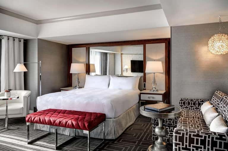 Luxurious hotel bedroom with white bedding, mirrored headboard, red bench, and contemporary furnishings