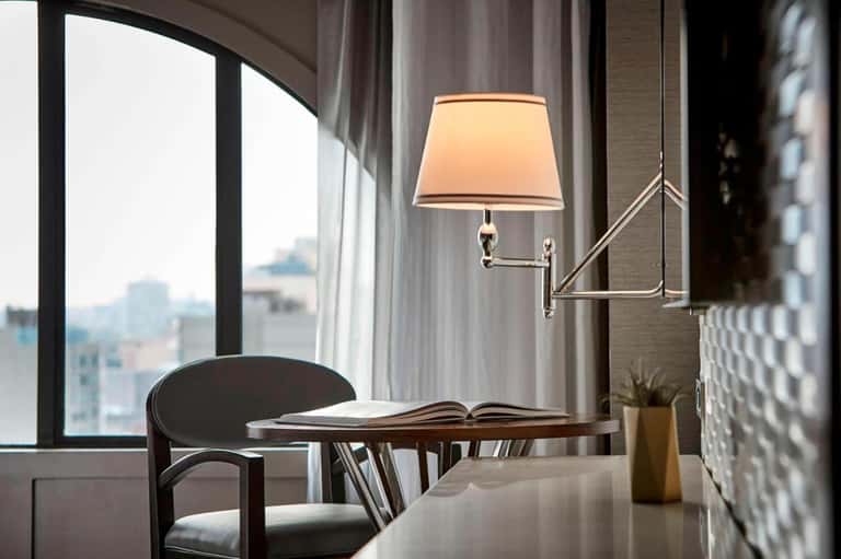 Elegant hotel room workspace with desk, modern lamp, and city skyline view through large window