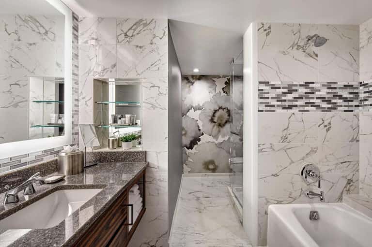 Marble bathroom with dual vanity sink, large mirror, walk-in shower, and white tub