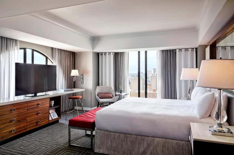 High-rise hotel bedroom with city views, modern furnishings, and flat-screen TV
