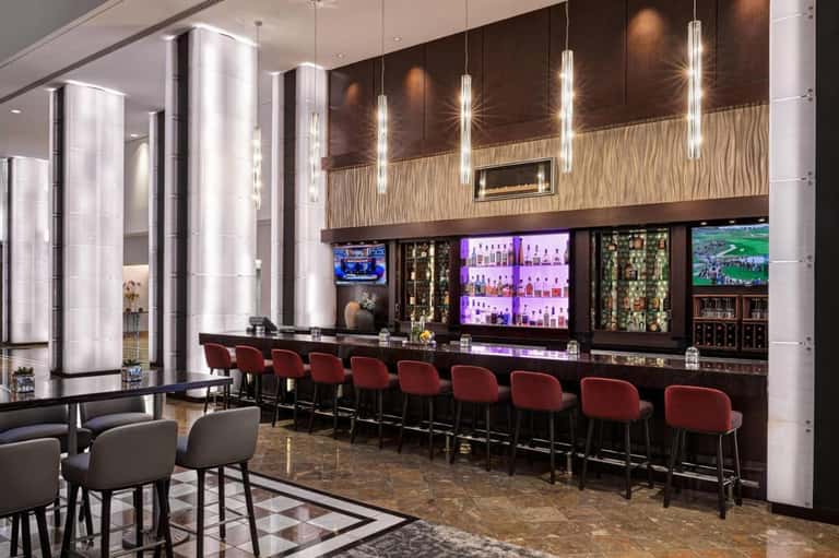 Upscale hotel bar with purple-lit liquor shelves, red bar stools, and flat-screen TVs
