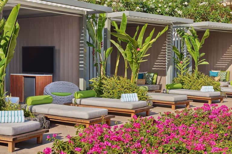 Outdoor lounge area with wooden daybeds, magenta flowers, and shaded pergolas near spa