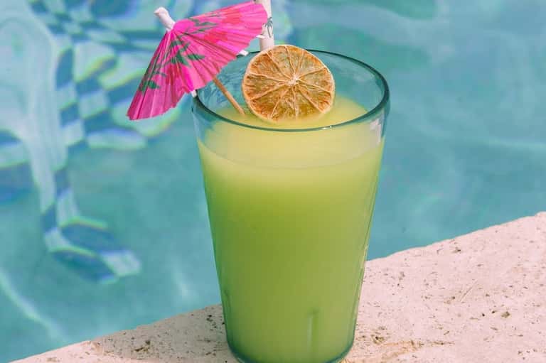 Tropical cocktail with pink umbrella and citrus slice by turquoise swimming pool
