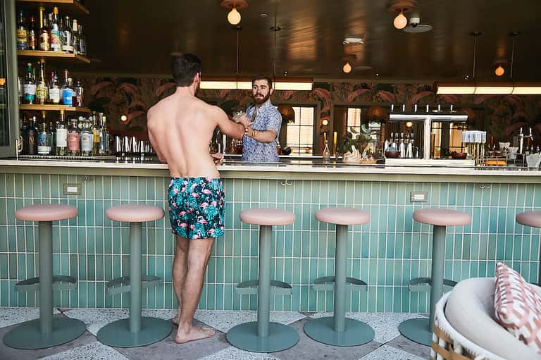 Beachside tiki bar with turquoise tile accents, man ordering cocktail, dark wood ceiling and tropical decor