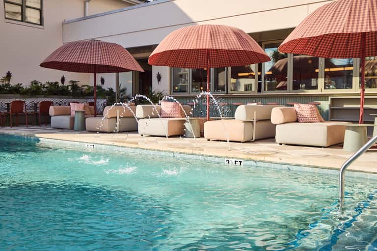 Pool area with red checkered umbrellas shading cream loungers and modernist seating