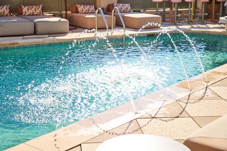 Resort pool with fountain features, lounge seating, and sunny courtyard area