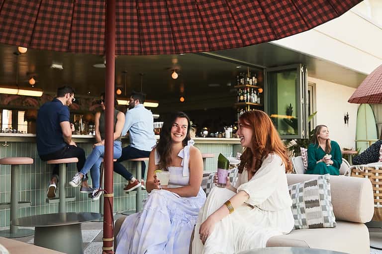 Outdoor bar and lounge area with red checkered umbrella and guests enjoying drinks