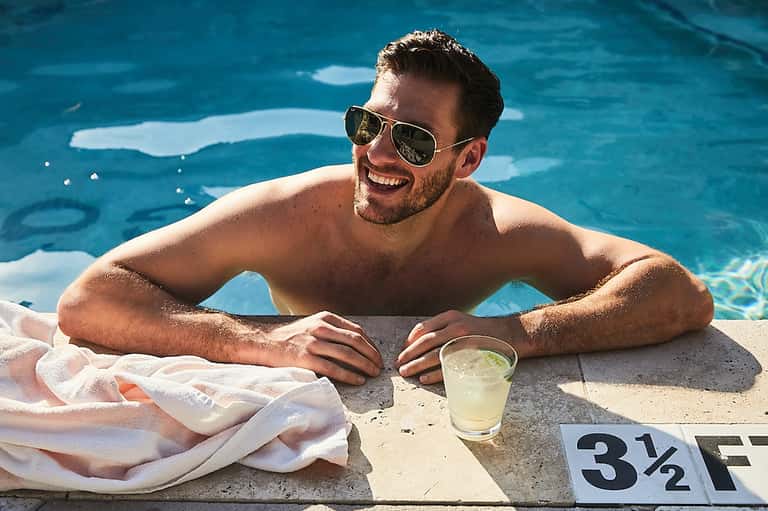 Man in sunglasses relaxing at pool edge with beverage and temperature sign showing 3½°F