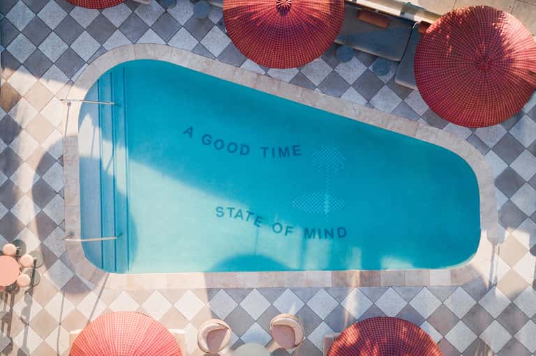 Overhead view of kidney-shaped pool with red umbrellas and checkerboard pavement