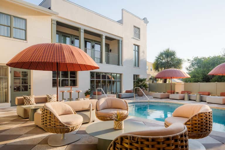 Outdoor pool area with loungers, red umbrellas, wicker seating, and modern architecture