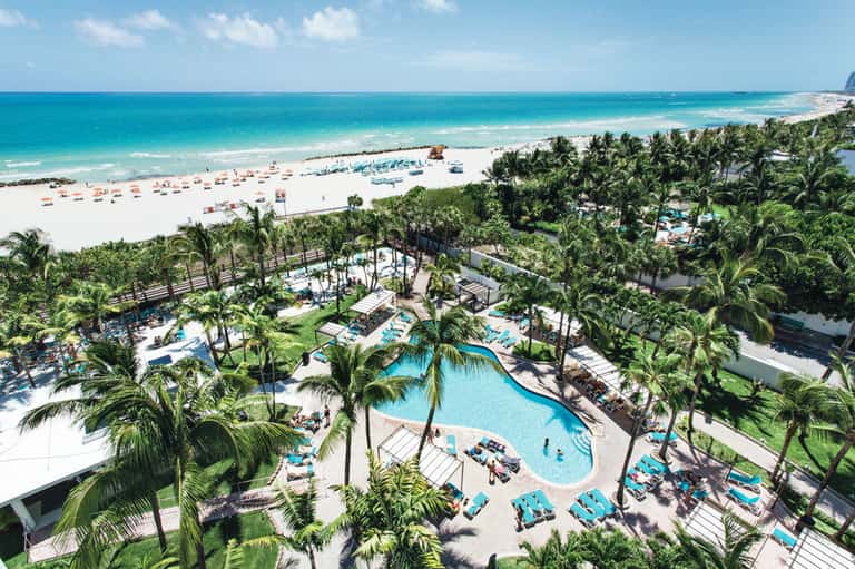Tropical beachfront resort pool surrounded by palm trees with beach and ocean view