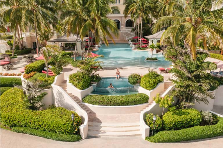 Luxurious courtyard with tiered pools, palm trees, manicured hedges, and beige architecture