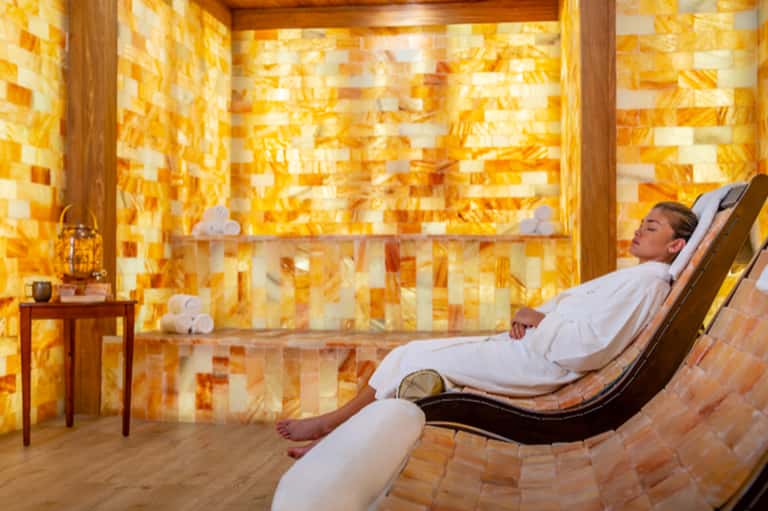 Man relaxing on lounge chair in spa salt room with glowing golden onyx tile walls