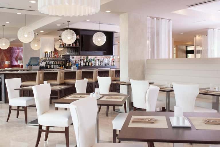 Modern restaurant interior with white chairs, dark tables, pendant globe lights, and full bar