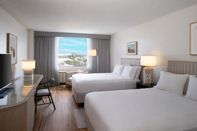 Modern hotel room with two queen beds, city view, desk, and contemporary furnishings