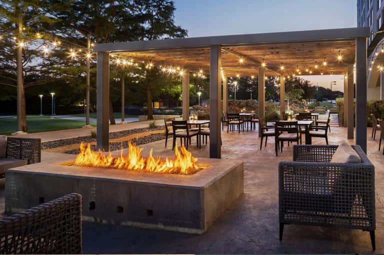 Covered patio with fireplace, dining tables, string lights, and lawn area at dusk