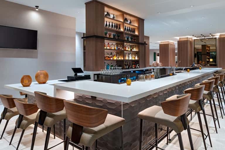 Contemporary bar with white counter, wooden chairs, and backlit liquor shelving
