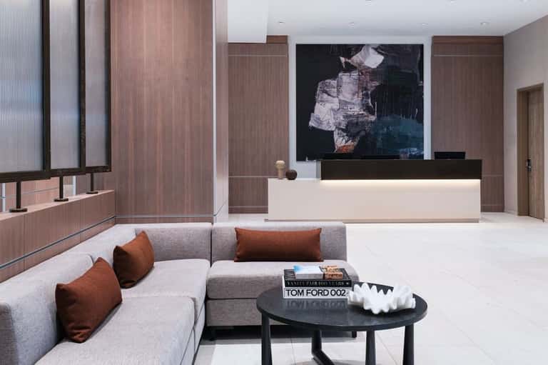 Modern hotel lobby with gray sectional sofa, wooden accent walls, abstract artwork, and minimalist reception desk
