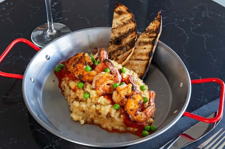 Shrimp risotto with grilled bread in red-handled pan on black marble surface