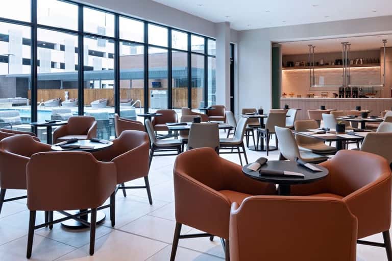 Modern hotel lounge with cognac leather chairs, floor-to-ceiling windows, and rooftop pool views