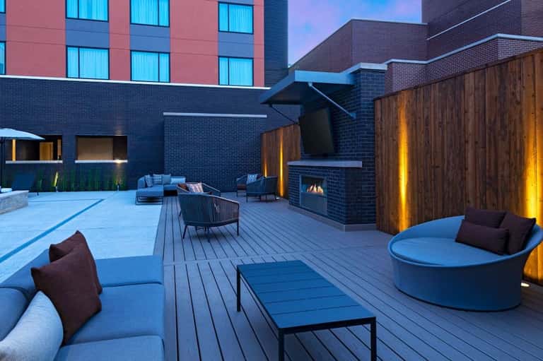 Contemporary rooftop terrace at dusk with seating areas, fireplace, wooden screens, and urban building backdrop
