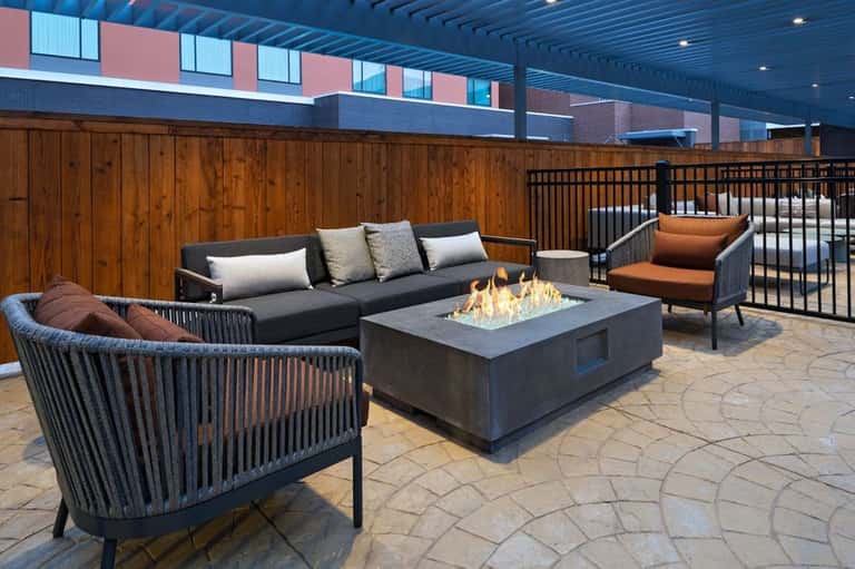 Rooftop lounge with fire pit, dark furniture, and city skyline views at dusk