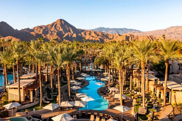 Desert resort with blue lagoon-style pool surrounded by palm trees and mountain backdrop