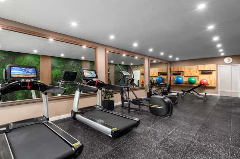 Modern fitness center with treadmills, exercise bikes, mirrors, and green accent wall
