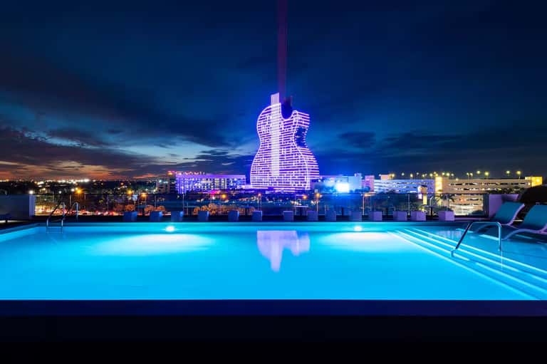 Rooftop pool glowing blue at night with illuminated guitar-shaped building landmark in background