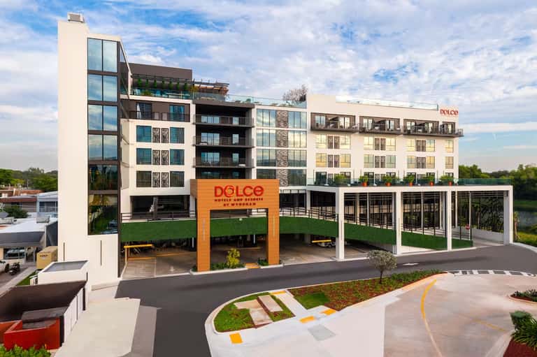 Modern mixed-use waterfront building with Dolce restaurant, orange signage, green landscaping, and residential apartments above