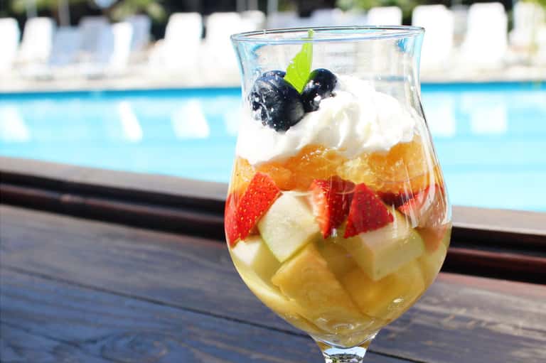 Colorful fruit punch with whipped cream, berries, and mint leaf garnish by poolside