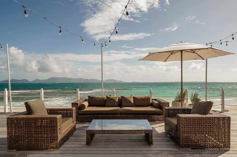 Beachfront lounge area with rattan furniture, umbrellas, and turquoise ocean backdrop