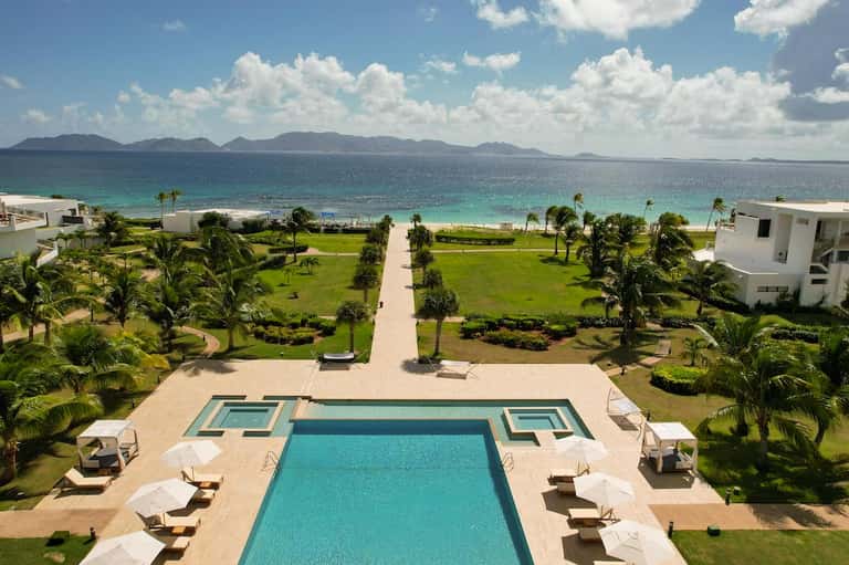 Beachfront resort aerial view with swimming pool, loungers, palm trees, and turquoise ocean