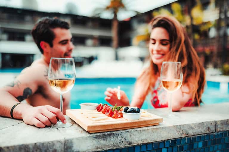 Couple enjoying wine and charcuterie by a resort pool at sunset