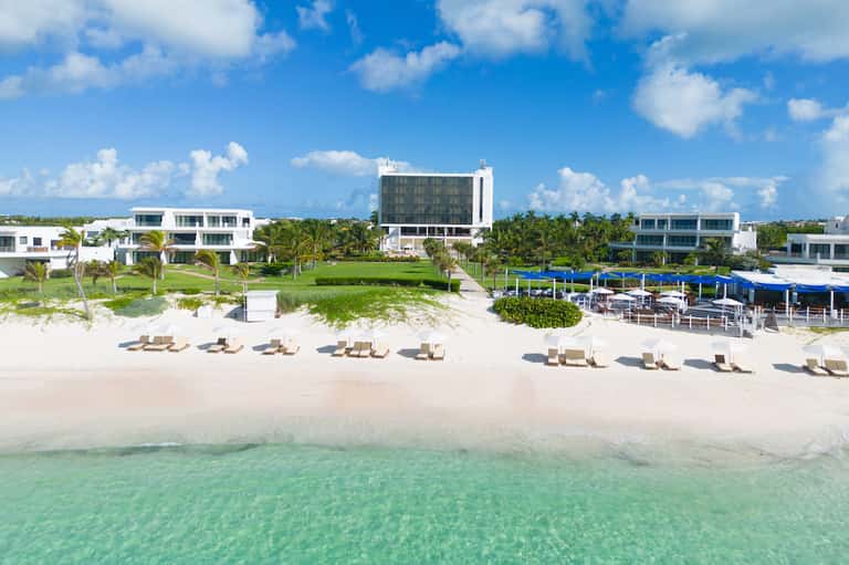 Beachfront resort with white sandy beach, lounge chairs, turquoise water, and modern white buildings