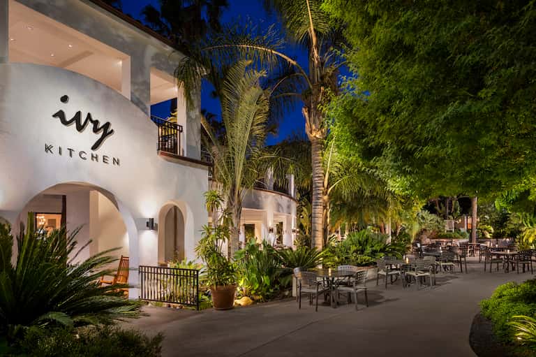 Ivy Kitchen restaurant exterior at night with white arches, palm trees, and outdoor seating