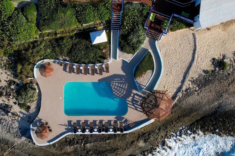 Aerial view of curved pool with lounge chairs and coastal landscaping