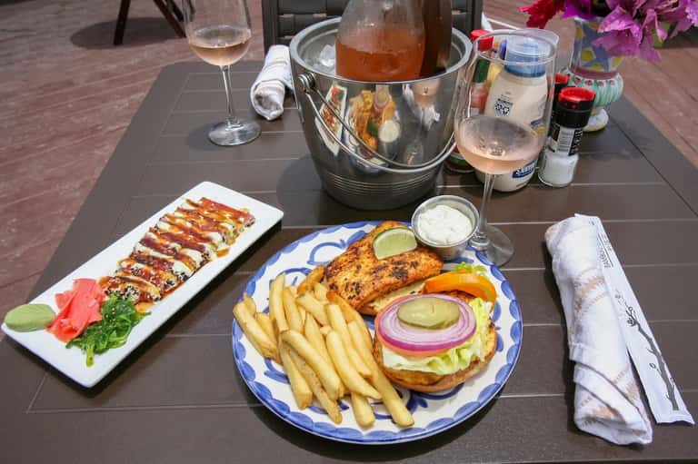 Outdoor dining table with sushi, grilled fish, fries, and beverages on dark surface