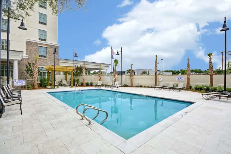 Resort outdoor swimming pool with lounge chairs, palm trees, and modern building architecture