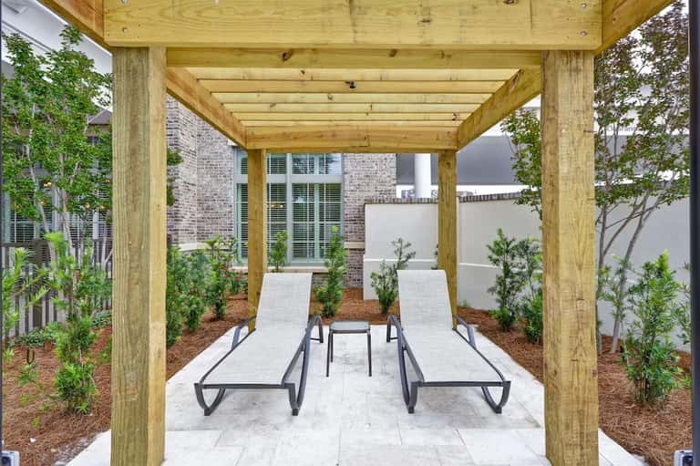 Wooden pergola covering loungers and seating area with potted plants and brick pathway in residential courtyard