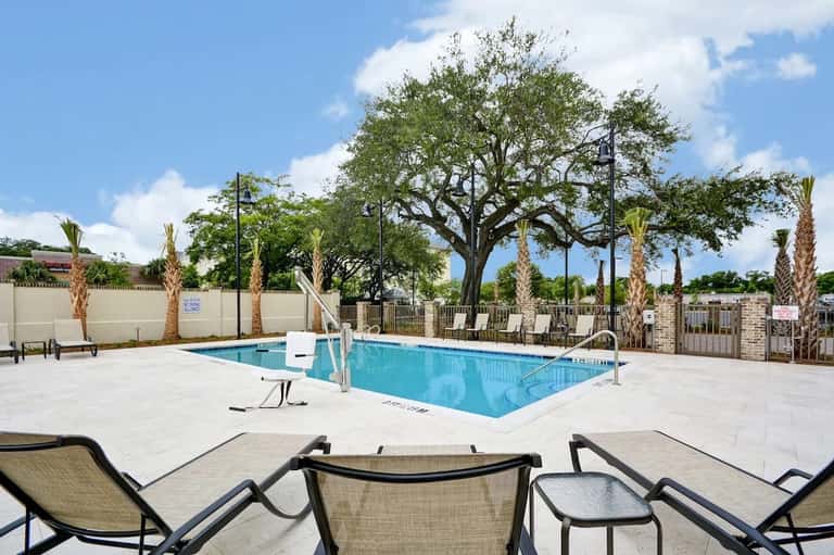 Resort swimming pool with lounge chairs, palm trees, and manicured landscaping under clear blue sky