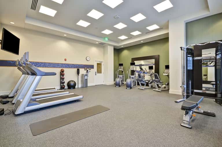Modern fitness center with treadmills, exercise bikes, and equipment on gray carpet flooring